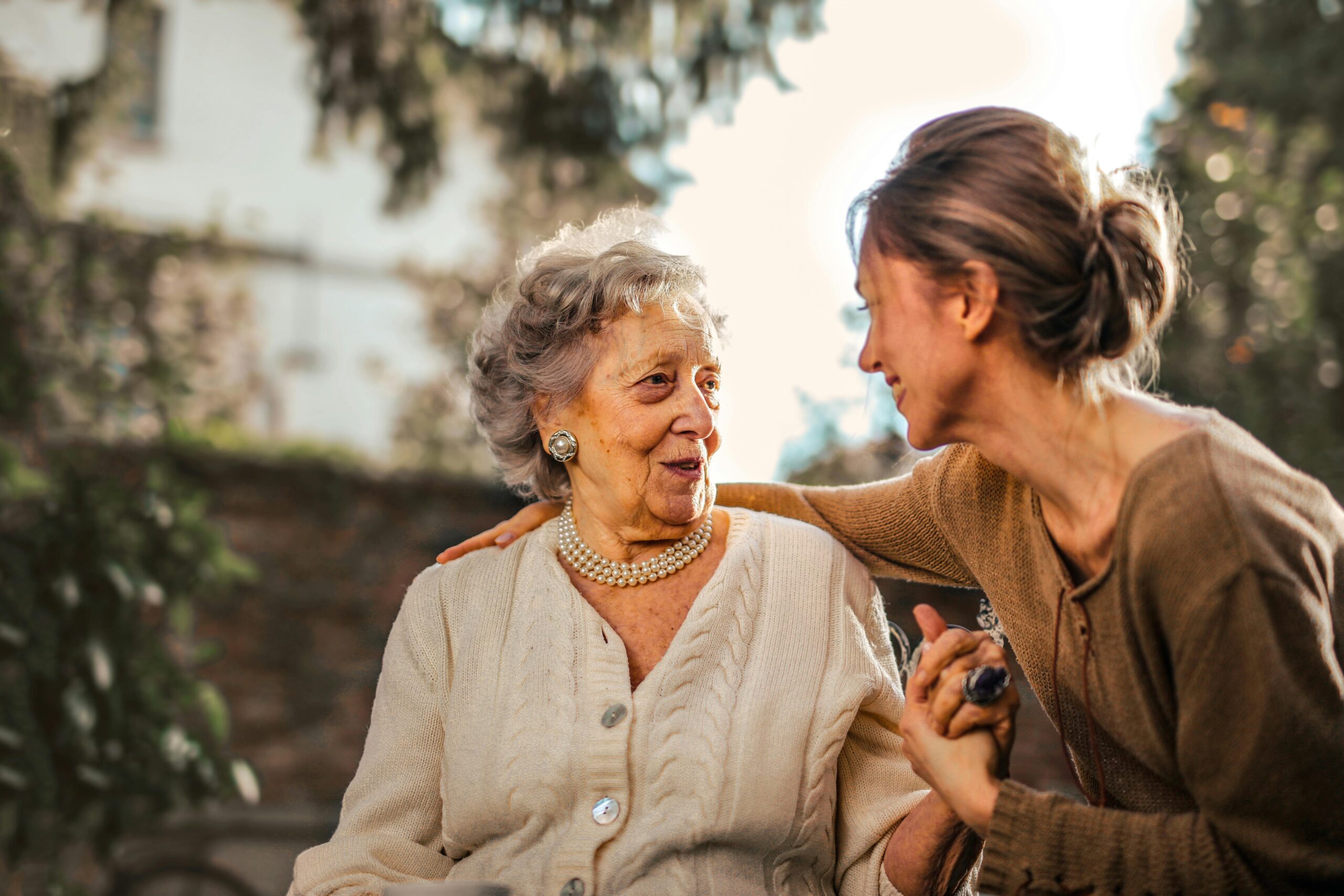 Home Elderly woman and adult daughter share a joyful, affectionate moment in a sunny garden.